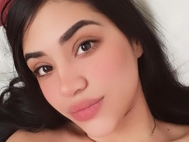 Le visage de SamanthaSweett, avec ses sourcils foncés, ses yeux marrons, ses lèvres roses et ses cheveux noirs, affiche un léger sourire et un léger blush rose sur ses joues. Ses fesses ne sont pas visibles..