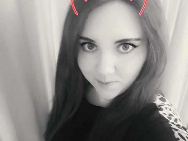MaryCrystal mit langem, dunklem Haar, die ein schwarzes Oberteil mit Leopardenmuster trägt, hat rote Teufelhörner auf dem Kopf und leicht geöffnete Lippen, die schwarzen Eyeliner zeigen..