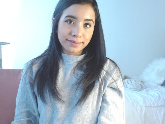 AshleyLover, con lunghi capelli neri, pelle color nocciola e un piercing al naso, indossa una felpa grigia e sorride dolcemente alla fotocamera. Il suo seno non è visibile..