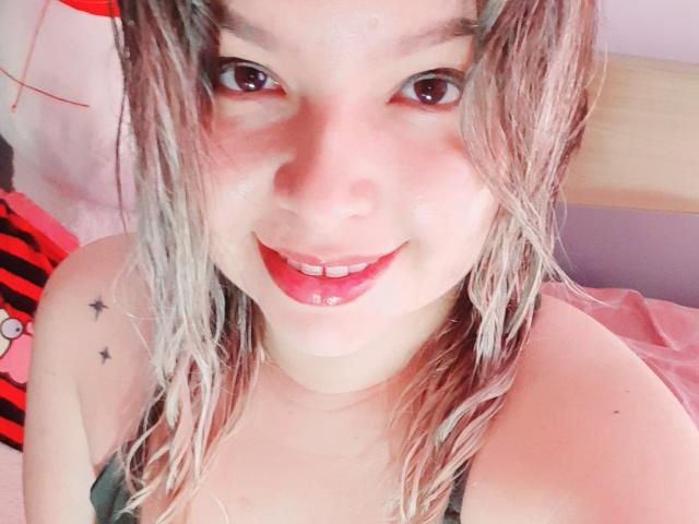 Myalewwis ha i capelli biondi e umidi, rossetto rosso e un sorriso che mostra i suoi seni lucidi. Ha piccoli tatuaggi a forma di stella sulla spalla. Il suo letto rosa è sullo sfondo..