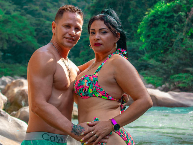 SashaYManuel con una mano tatuata sul sedere, che indossa un bikini colorato a fiori, e un SashaYManuel senza maglietta con i glutei a forma di Calvin, in piedi in una foresta rocciosa e verde..