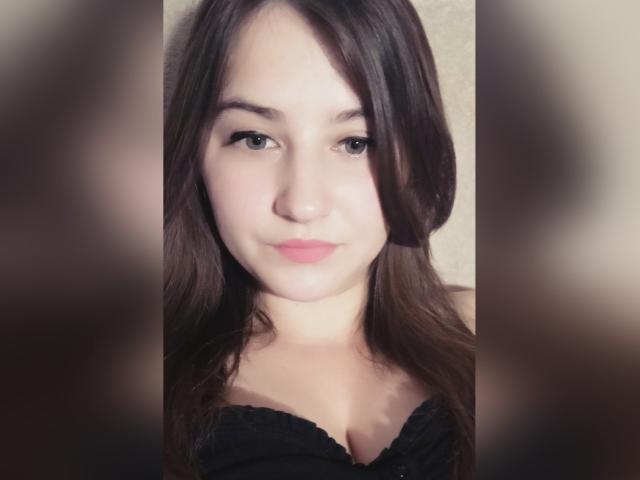 MiraDickey, met bruin haar, lichte huid en roze lippen, draagt een zwarte kanten top, waardoor haar kleine borsten zichtbaar zijn, en ze heeft een subtiele glimlach, gecentreerd in de afbeelding..