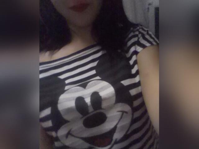 MiraDickey con una camicia a righe bianche e nere con un'immagine grande di Topolino, che mostra il suo seno, rossetto scuro e capelli neri ondulati, in una foto leggermente sfocata..