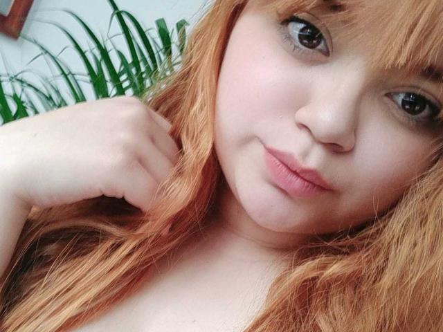 Allie Johnson, con la pelle chiara, i capelli rossi e le labbra piene, si tiene i capelli indietro, mostrando gli occhi marroni e un leggero sorriso, in un selfie. Il suo seno è parzialmente visibile..