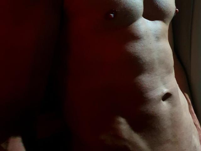 LustyLover's slim, toned, dark-skinned torso with small, firm boobs and a visible navel under dim, red lighting.
