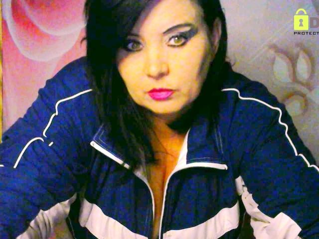 KamilaDream mit dunklem Haar, pinkem Lippenstift und dicker schwarzer Eyeliner, trägt eine blaue und weiße Jacke mit Reißverschluss und blickt mit ernstem Gesichtsausdruck direkt in die Kamera..