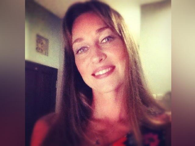 LilyOCute tem cabelos castanhos longos, olhos azuis e um sorriso discreto com batom rosa. Ela está vestindo uma blusa vermelha, e a foto tem um filtro suave e ligeiramente borrado..
