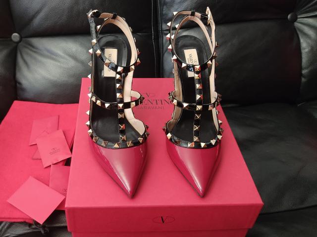 A pair of hot pink, pointed-toe stiletto heels with black and silver studs, placed on a pink box, surrounded by pink tissue paper. AlfaFemale's shoes.