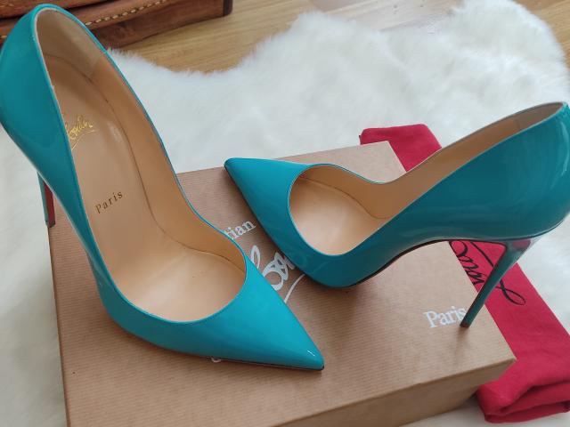 Teal stiletto heels with pointed toes and high heels, lying on a beige box, next to a red cloth, on a white fur rug. AlfaFemale's sexy shoes.