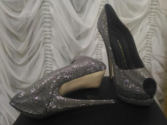 Shiny silver high heels with a peep-toe design, covered in tiny sparkling rhinstones, and a beige heel, positioned on a black surface. AlfaFemale's ass is nowhere.