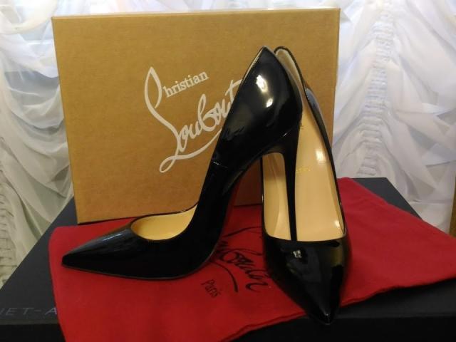 Black glossy stiletto heels with pointed toes, resting on a red cloth, next to a brown box. Box has white "Louboutin" logo. AlfaFemale's sexy shoes, ass-kicking style.