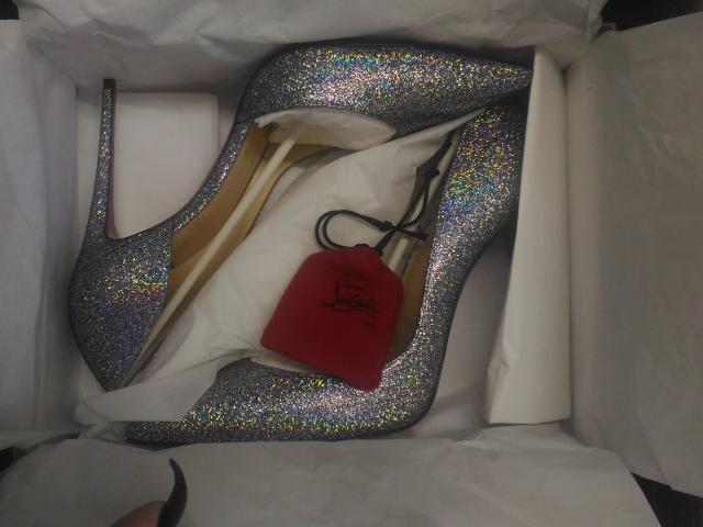 Salto alto prateado brilhante com glitter multicolorido, dentro de uma caixa branca com uma etiqueta vermelha da Louboutin e forro bege, com bicos pontudos e tiras pretas..