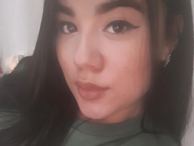 SteffanyTaylor has dark brown hair, thick eyebrows, and wears eyeliner. Her full lips are slightly pouted. She's wearing a green top and has small, silver earrings.