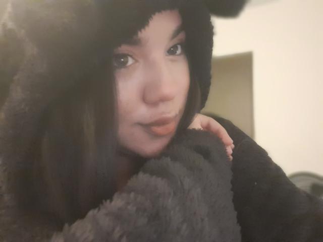 Steffany Taylor, con i capelli castano scuro, indossa un cappello nero e soffice e un cappotto abbinato, abbraccia un peluche nero, guardando leggermente di lato con un sorriso appena accennato..
