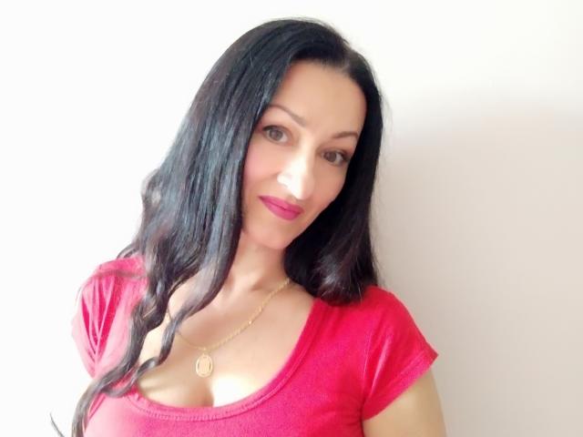 Antralyn, con cabello negro largo, una camisa roja y un collar dorado, aparece en un selfie mostrando sus senos. Está sonriendo con lápiz labial rosa, luciendo linda y sexy..