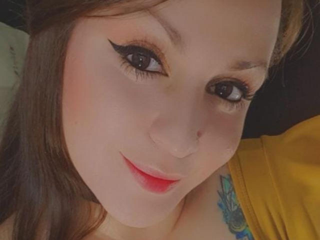 ElinaJhonson's face with thick black eyeliner, red lipstick, and a subtle smile. She has light skin, brown hair, and a small tattoo on her right shoulder.