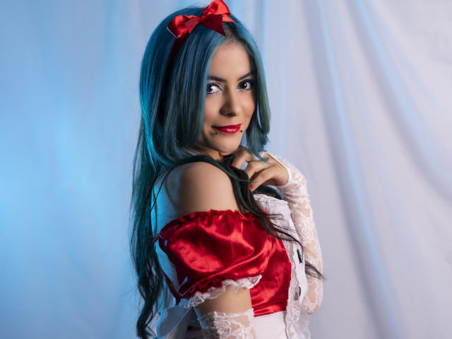 CandiceValo avec des cheveux bleus, un nœud rouge et une robe rouge à une épaule, regardant par-dessus son épaule, souriante, rouge à lèvres rouge, manches en dentelle, fond blanc, main sur la poitrine, mignonne, sexy..