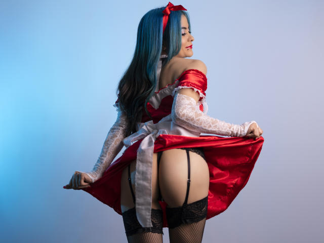 CandiceValo with blue hair, red dress, white lace gloves, and black lace stockings, lifting dress to expose her bare ass and black garter. She's wearing a red ribbon in her hair.