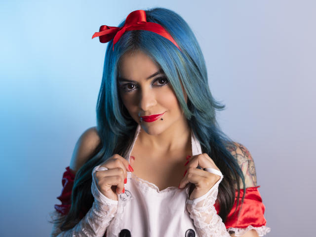 CandiceValo with blue hair, red headband, white lace dress, holding straps, red lipstick, tattoos on right arm, smiling, red nails, medium breasts, cute, sexy, photograph.