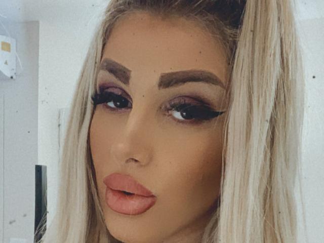 TanyaMonroe has blonde hair, full pink lips, and thick black eyeliner with long lashes. Her eyebrows are dark and well-groomed, with subtle purple eyeshadow.