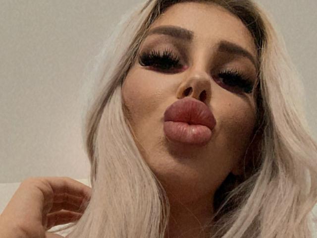 TanyaMonroe's face with pouty pink lips, long blonde hair, and heavy eyelashes, looking down with a hand near her head, showing off her sexy, full lips.