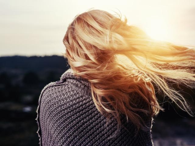 KaraWill with long blonde hair, wearing a gray knitted sweater, back to the camera, sun flaring through her hair, looking like a sexy, pretty, hot blonde chick.