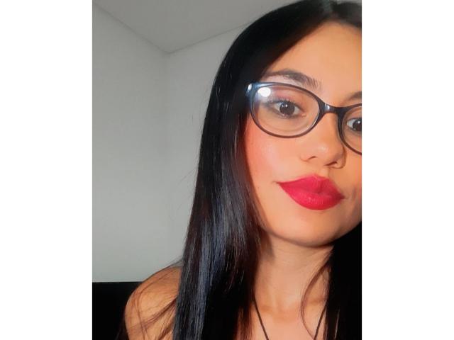 LolyFunX has long black hair, wears glasses, and has red lipstick on her plump ass. Her brown eyes are looking at the camera with a slight smile.