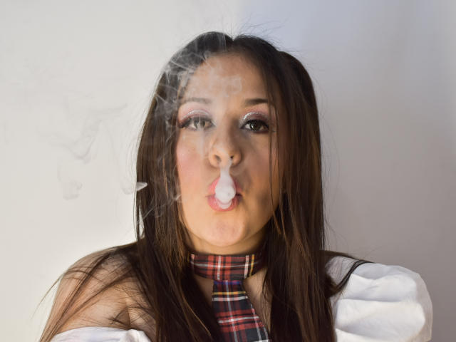 KatieWoolf a du sperme sur son visage et dans sa bouche, elle porte une cravate à carreaux, une chemise blanche, et ses cheveux bruns sont attachés en couettes..