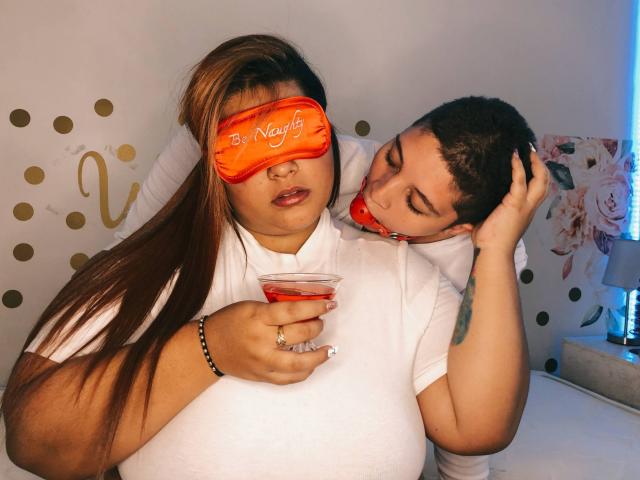 Susan y Jostin, con cabello castaño largo, camisa blanca y antifaz naranja, sosteniendo una bebida. Jostin, con cabello castaño corto y una bandana roja, le roza el cuello. Ambas parecen relajadas..