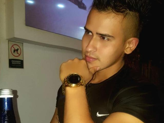 AngelLin, avec ses cheveux courts et foncés, sa peau mate, et son t-shirt noir Nike, se tient la main au menton, portant une montre en or, et a l'air légèrement agacé, avec une bouteille de bière devant lui..