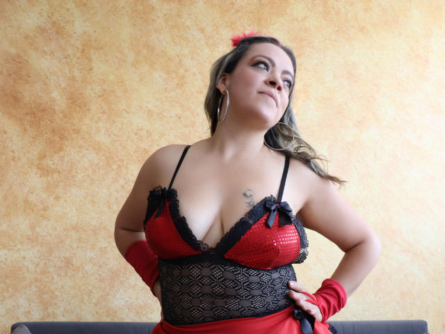 LiliCarina with big tits, red lace bra, black mesh, red gloves, and a pink hairclip, looking up with a confident smile, hands on hips.