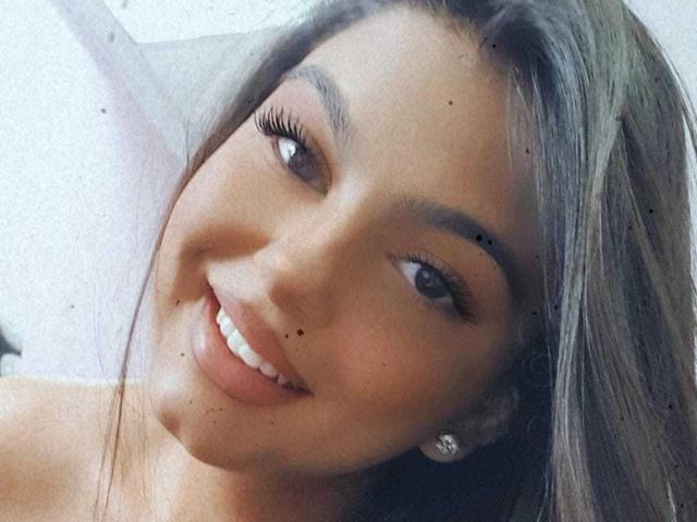 Beckyte's smiling face with long, straight, grayish-brown hair, brown eyes, and small moles on her cheek and chin, wearing diamond earrings, showing her white teeth.