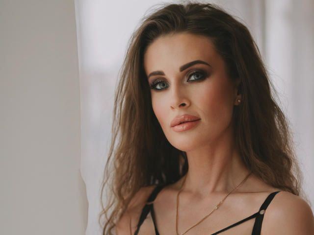 MikaFetish tiene el pelo largo y castaño, ojos verdes y labios rosados y carnosos. Lleva un top negro con tirantes y un collar dorado. Su trasero no es visible..
