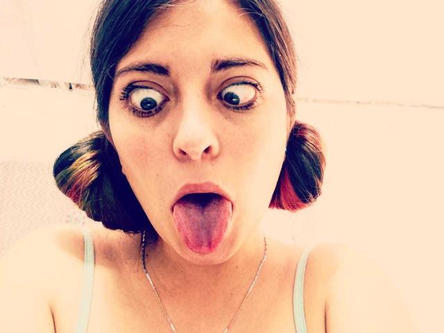 BrightLightz has wide eyes and a tongue out, with short, dark brown pigtails featuring red highlights. She's wearing a light blue top and a thin necklace.