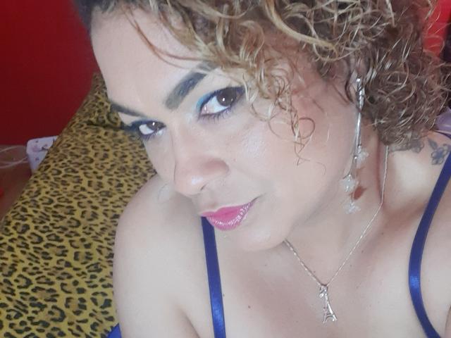 SolmaryHot with curly blonde hair, blue eyes, and pink lipstick, wearing a blue bra, has cum on her cheek, and a tattoo on her right shoulder.