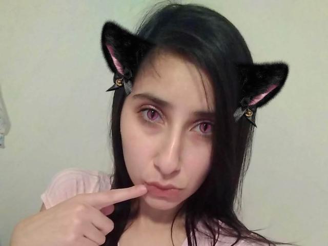 Nico Robin com orelhas de gato pretas, olhos rosa e cabelo preto, fazendo beicinho com o dedo nos lábios, vestindo uma camisa rosa, com uma aparência sexy e fofa, e com um tom de pele claro..
