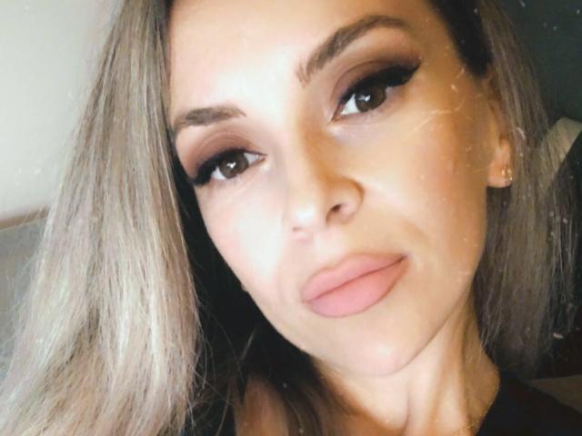 SophieDeee has puffy ass-shaped lips, thick black eyeliner, and brown eyes with subtle makeup. Her blonde hair is straight, and she's wearing small gold earrings.