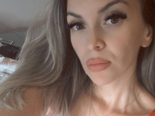 SophieDeee has long blonde hair, full eyebrows, and pouty pink lips. She's wearing a thin necklace, and her makeup includes long lashes and subtle eyeshadow.