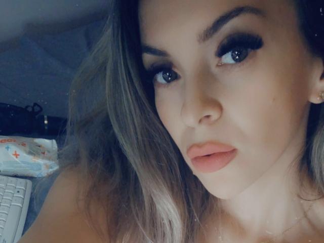SophieDeee's face with full lips, dark eyebrows, long eyelashes, and blonde hair, looking directly at the camera with a slightly pouty expression. Her boobs are not visible.