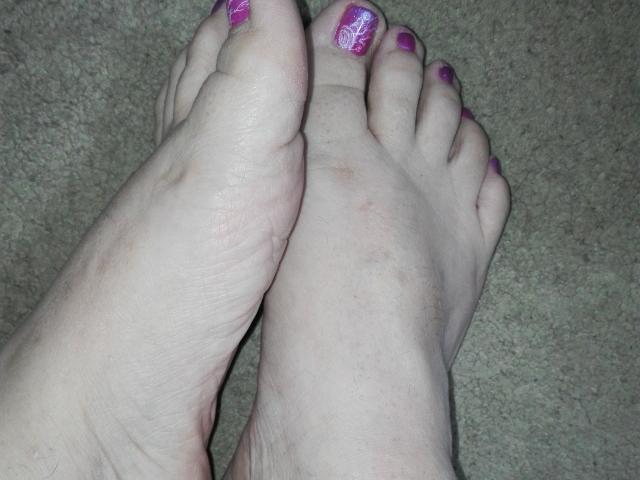 Les pieds de ces femmes latino, avec du vernis à ongles violet, les orteils légèrement recourbés, debout sur un tapis. Les plantes des pieds sont visibles, les orteils pointant vers le haut. Peau pâle, avec une légère teinte rosée. Pas de tatouages ou de marques visibles..