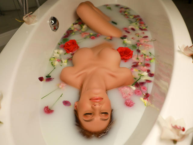Julia Richard, nackt, mit Brüsten und einem Nasenpiercing, liegt in einer weißen Badewanne, die mit Wasser und Rosenblättern gefüllt ist, die Beine verschränkt, und starrt in die Kamera..