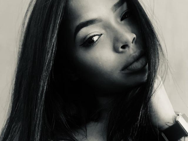 VickyGreys has dark, long hair, full eyebrows, and a slightly parted lip with a serious expression. She's wearing a watch on her right wrist in a black-and-white photo.