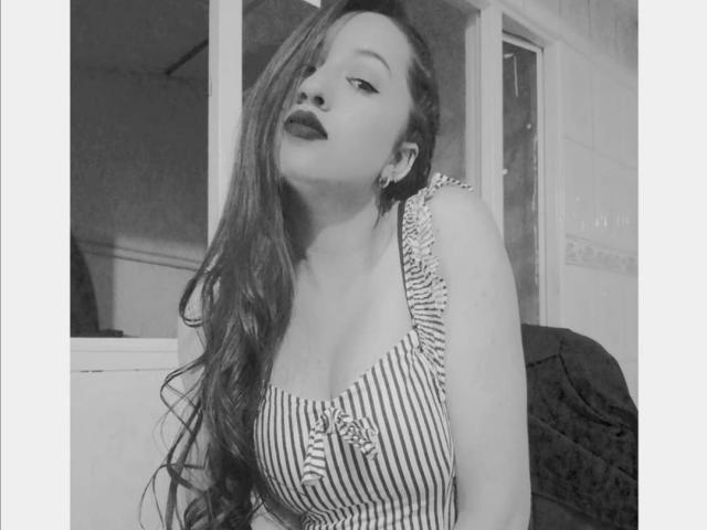Fotografia in bianco e nero di Isabella Wang con capelli lunghi e ondulati, vestito a righe e scollatura profonda, testa leggermente inclinata, rossetto scuro e orecchini, che la ritrae in modo seducente..