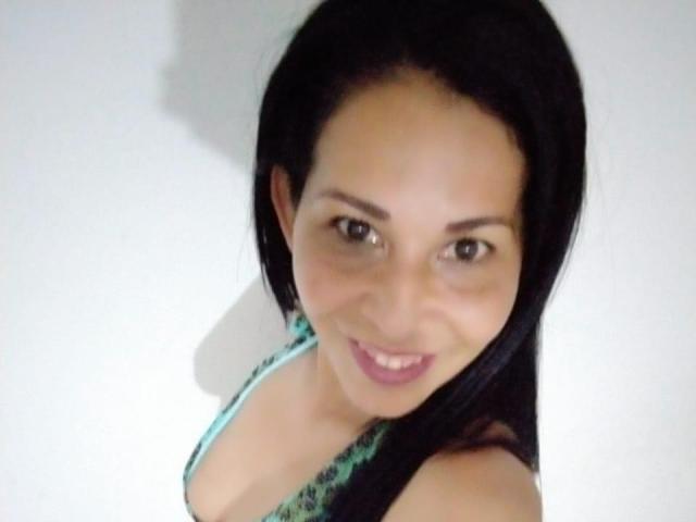 A ShanonMature tem cabelo escuro, olhos castanhos e um sorriso adorável. Ela está vestindo uma blusa com estampa verde, que revela seus pequenos seios. Ela está olhando para a câmera..