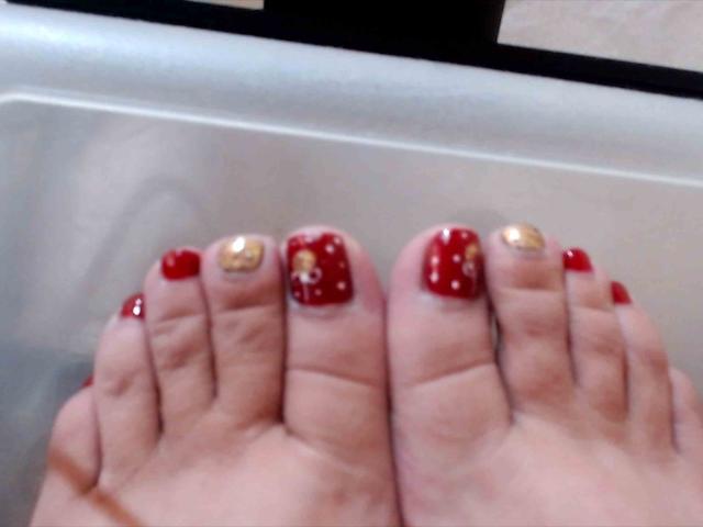 Les pieds de MistresSara, avec des orteils peints en rouge et un orteil peint en or sur chaque pied, montrent du rouge avec des points blancs et de l'or avec de petits points jaunes sur les orteils du dessus..