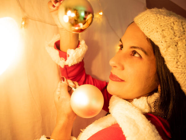 RoraimAnaggie with a cute face, holding a shiny silver ball and a white Christmas ornament, wearing a red and white fur-trimmed coat, and a knitted white hat.