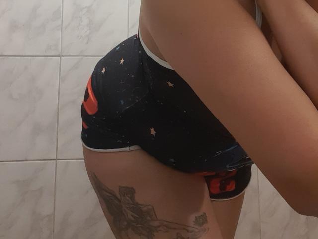 SolmaryHot mostra il suo sedere indossando dei pantaloncini blu scuro aderenti con stelle rosse e gialle, rivelando un tatuaggio sulla coscia destra. Ha le braccia incrociate, che coprono parzialmente il petto..