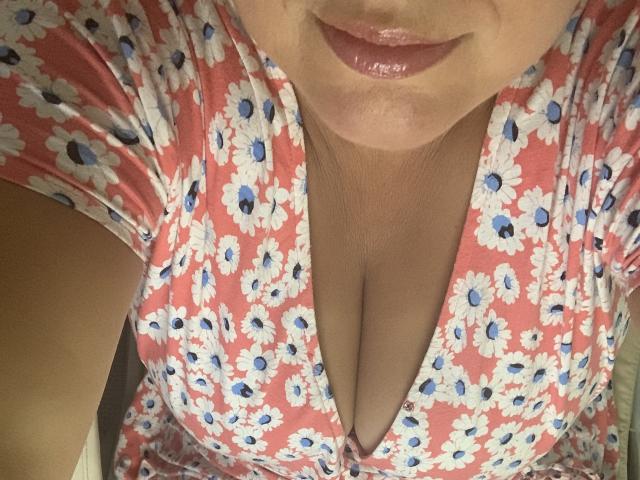 DearLola's pink floral dress with blue centers, showing her cleavage and glossy pink lips, focusing on her chest and part of her face, taken from a top-down angle.