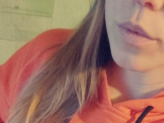 DorrieAnn's face, showing her pink lips and slightly parted mouth, with long brown hair, wearing a red hoodie, visible from the neck up in a selfie.