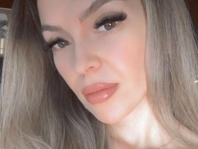 SophieDeee has shiny, pouty lips, long eyelashes, and smooth skin. Her blonde hair and raised eyebrows give her a sexy, confident look. Her brown eyes are slightly upturned.